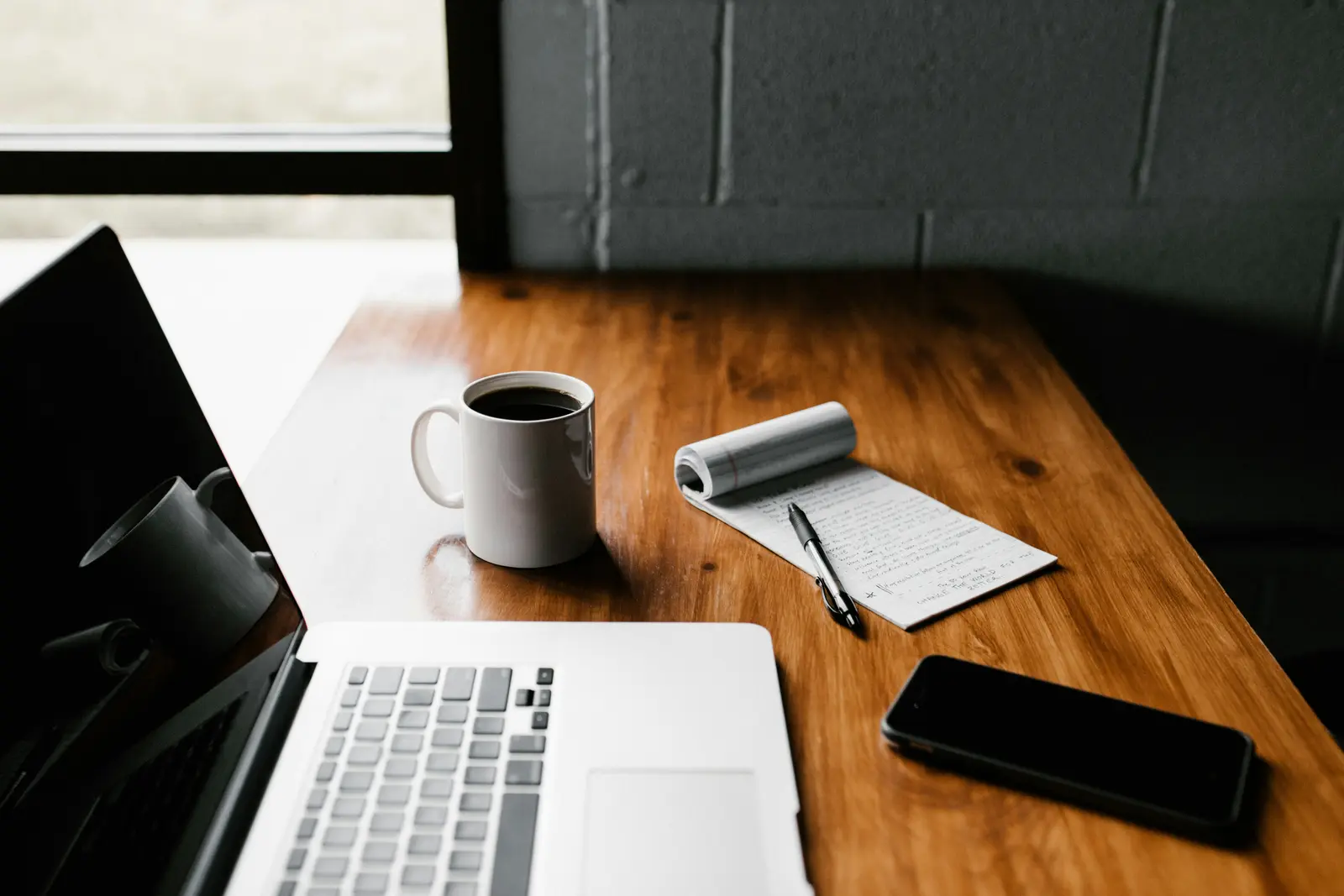 A laptop, phone and coffee mug on a desk workspace